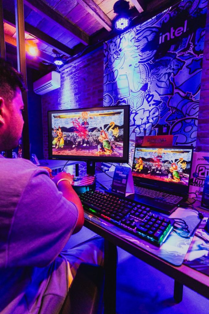 A gamer focused on a colorful battle game at a tournament setup with multiple screens.
